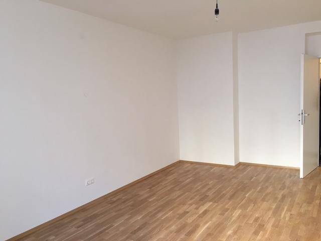 Helles, leeres Zimmer mit Holzboden und weißen Wänden, bereit zur individuellen Gestaltung.