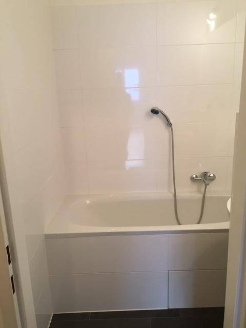 Badezimmer mit einer eingebauten Badewanne und weißen Wandfliesen sowie dunklem Boden.