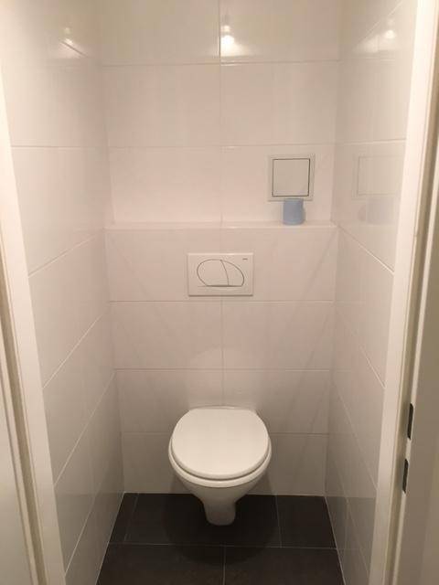 Kleines, hell gefliestes Gäste-WC mit wandhängender Toilette und dunklem Boden.