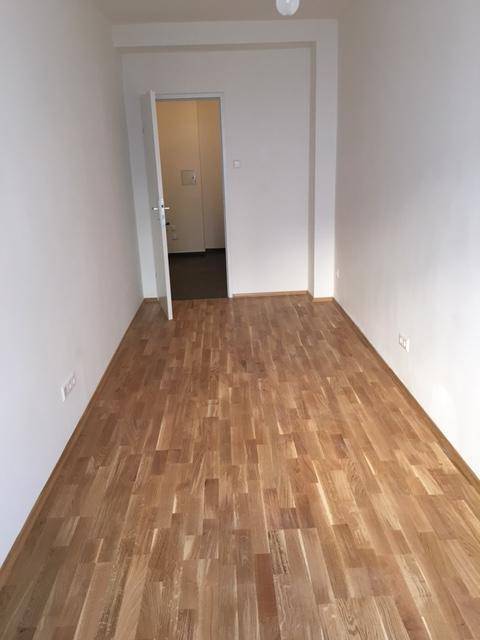 Leeres Zimmer mit Parkettboden und Zugang zu einem weiteren Raum mit Fliesenboden.
