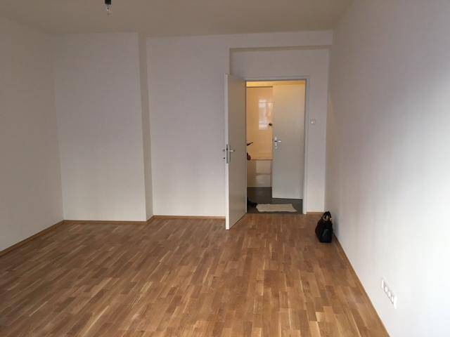 Leeres Zimmer mit Parkettboden und Zugang zu einem weiteren Raum mit Fliesenboden.