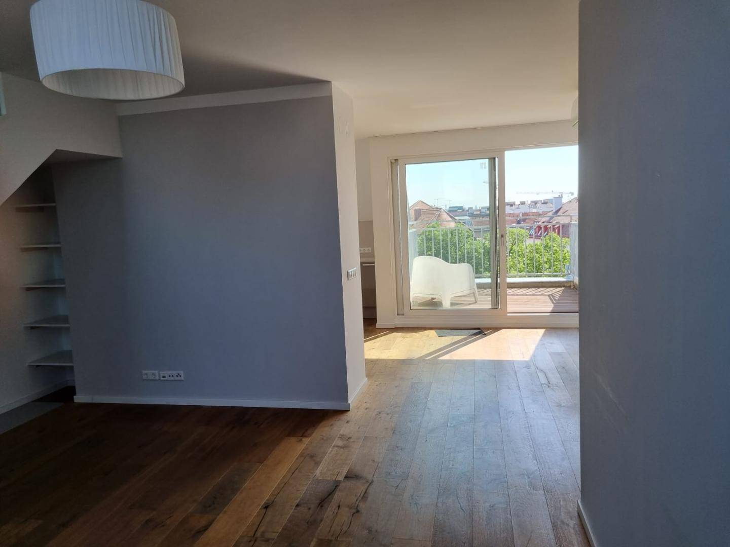 Helles Wohnzimmer mit Holzboden und Zugang zu einem sonnigen Balkon oder einer Terrasse.
