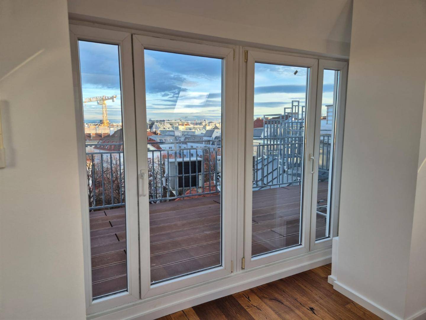 Innenraum mit Holzboden und großen Fenstertüren, die auf einen Balkon mit Stadtblick führen.