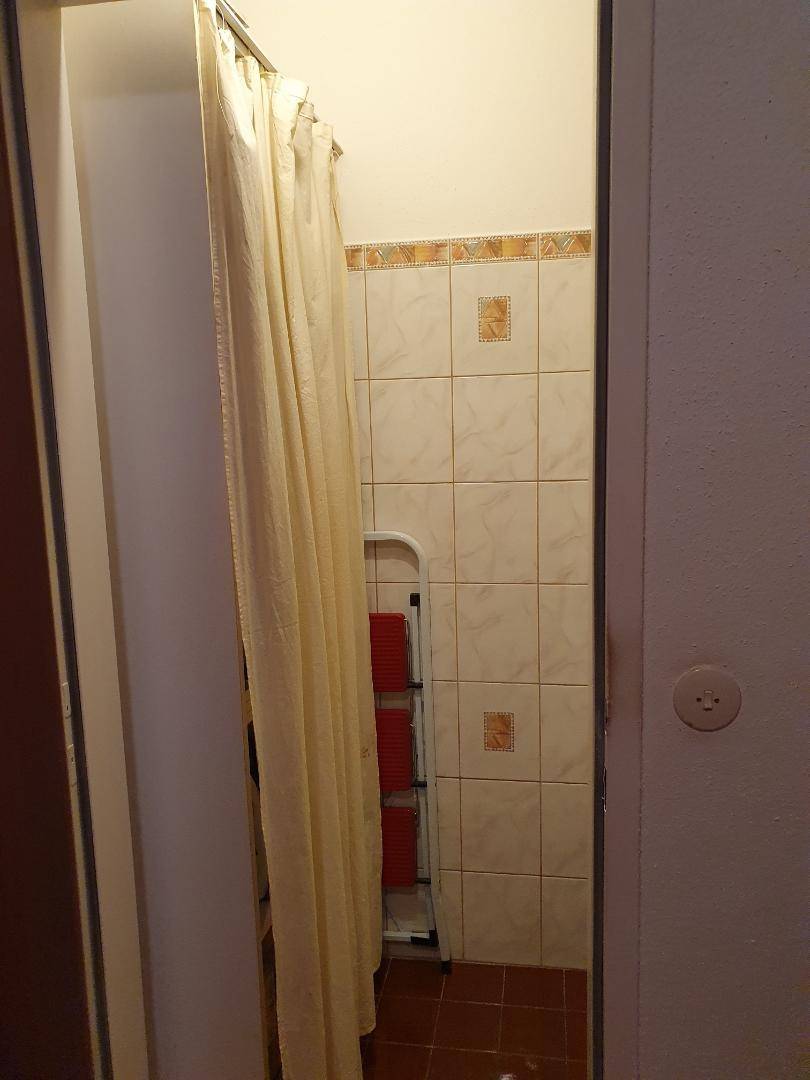 Kleine Duschkabine mit beigen Fliesen und Duschvorhang in einem funktionalen Bad.