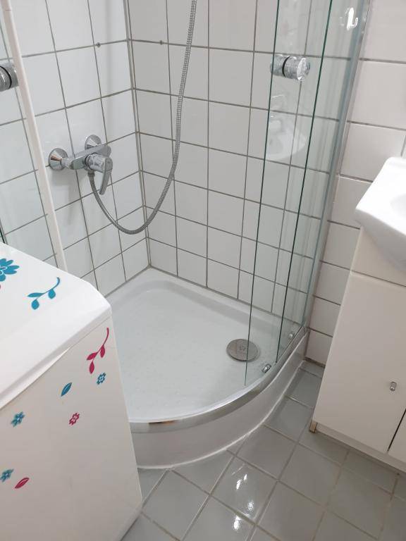 Badezimmer mit einer Eckdusche und einem kleinen Waschbeckenunterschrank, alles in hellen Fliesen.