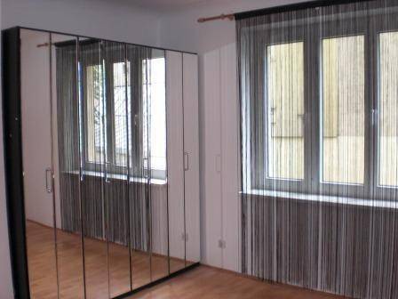 Heller Raum mit großem Spiegelschrank und Fenstern mit dunklen Vorhängen.