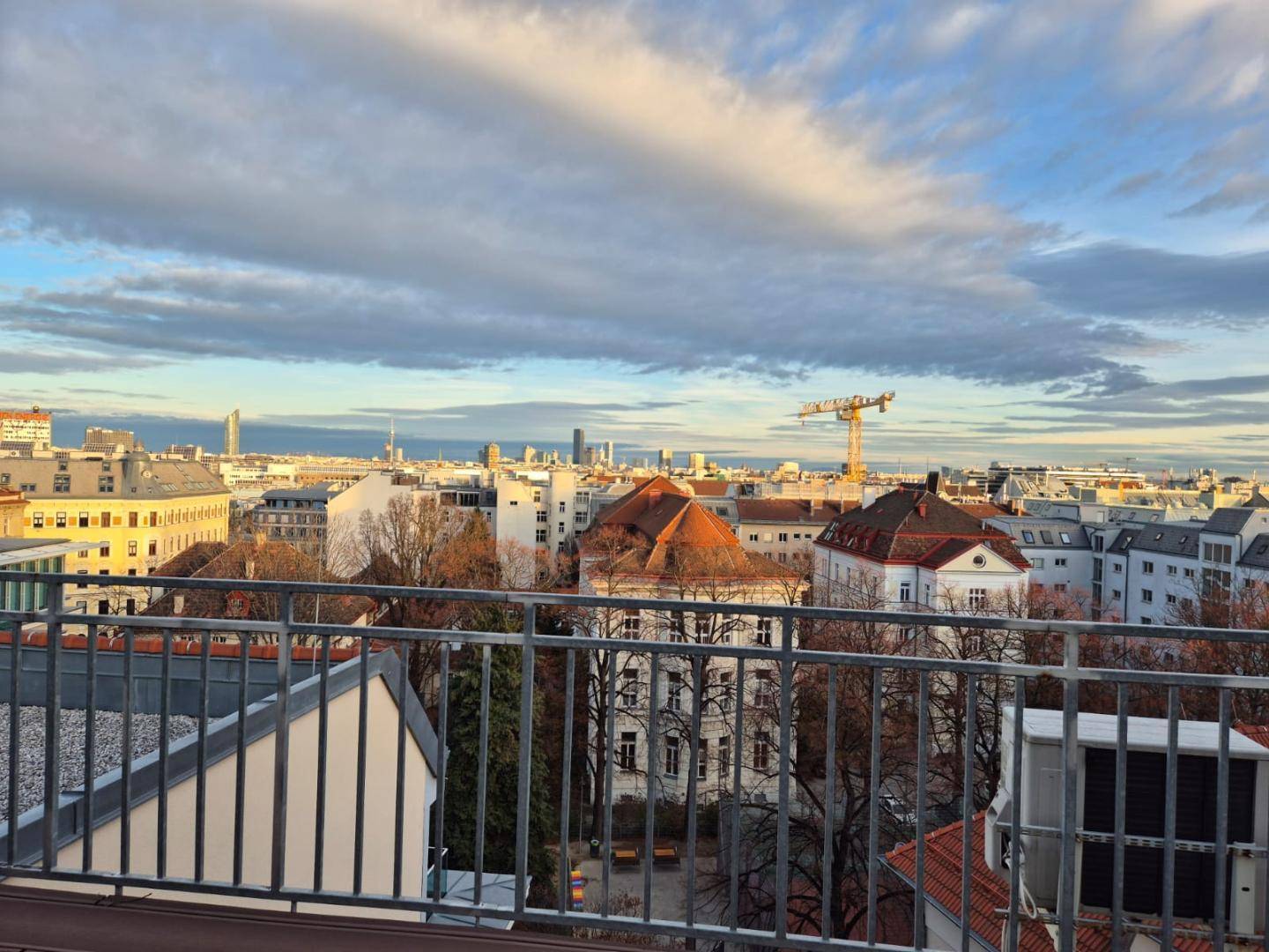 Weitläufiger Stadtblick von einer Dachterrasse mit Dächern und einem bewölkten Himmel.
