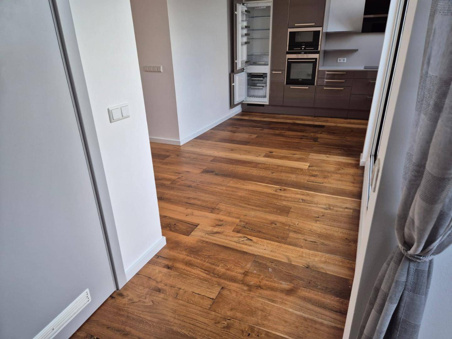 Heller Flur mit Holzboden und Blick auf die moderne Küche, durch eine Tür getrennt.