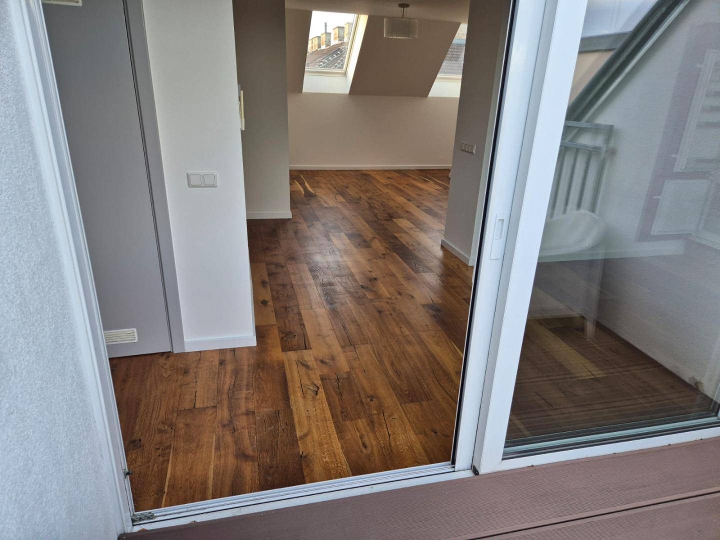 Blick vom Balkon in einen hellen Raum mit Holzboden und Dachfenstern.