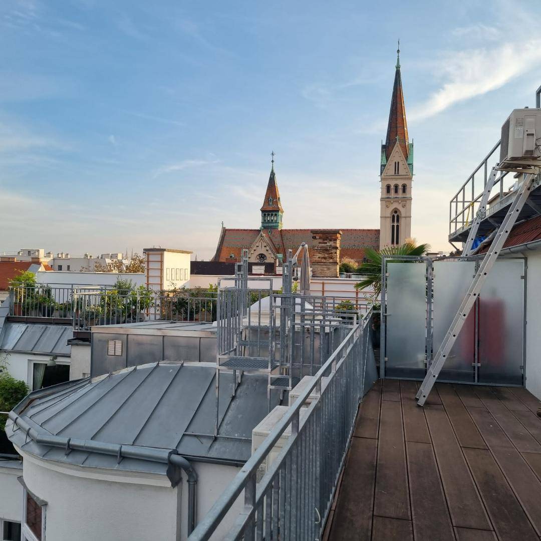 Dachterrasse mit Holzboden und Blick auf eine historische Kirche in der Ferne.