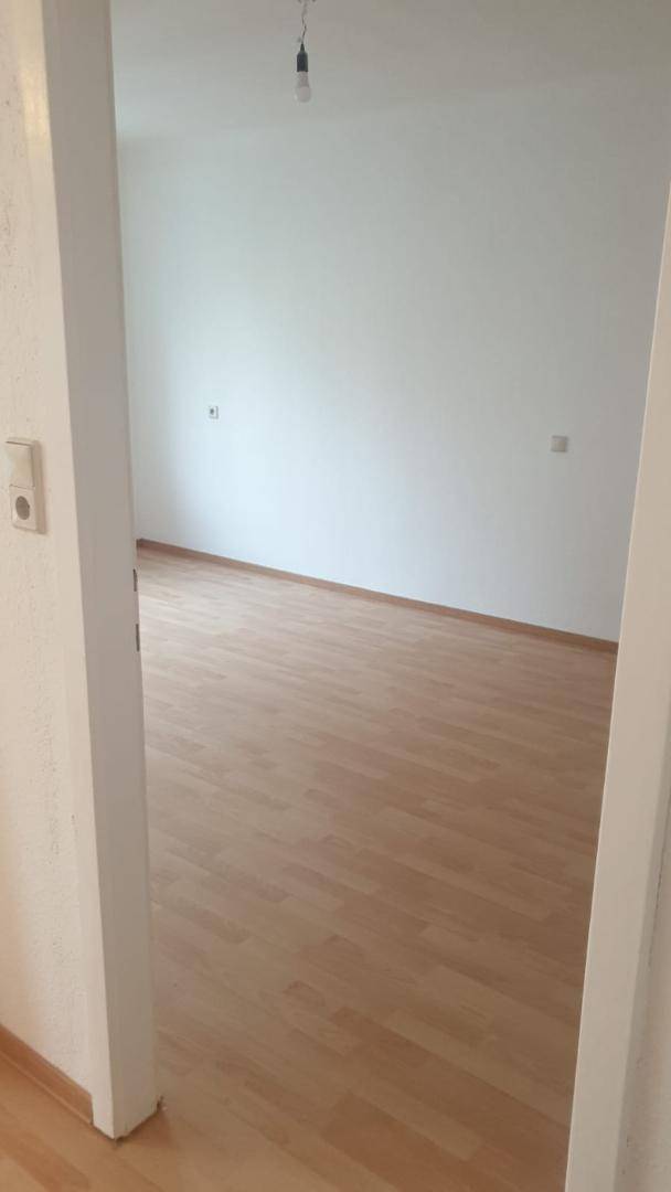 Leerer Raum mit hellem Laminatboden und weißen Wänden, bereit zur individuellen Gestaltung.