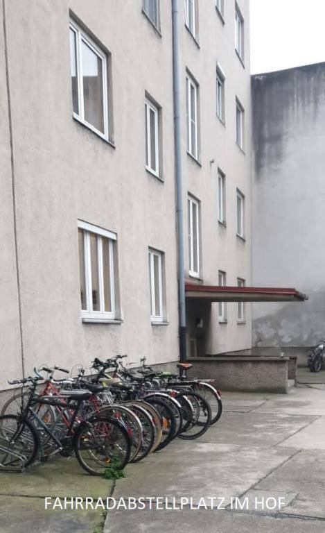 Fahrradabstellplatz im Hof eines Gebäudes mit mehreren Fenstern und schlichter Fassade.
