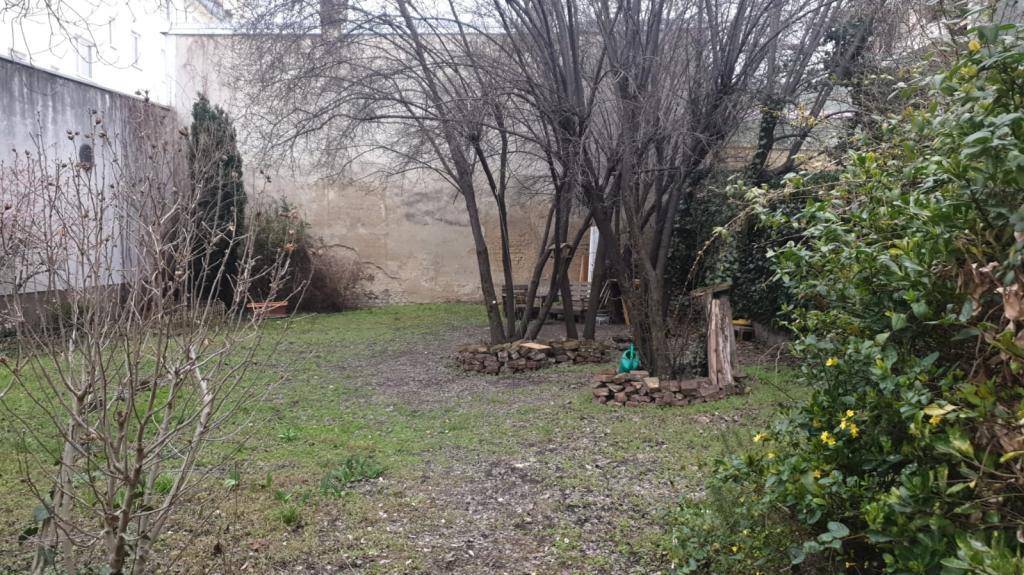 Gartenbereich mit Rasenfläche, mehreren Bäumen und einer kleinen Sitzecke im Freien.