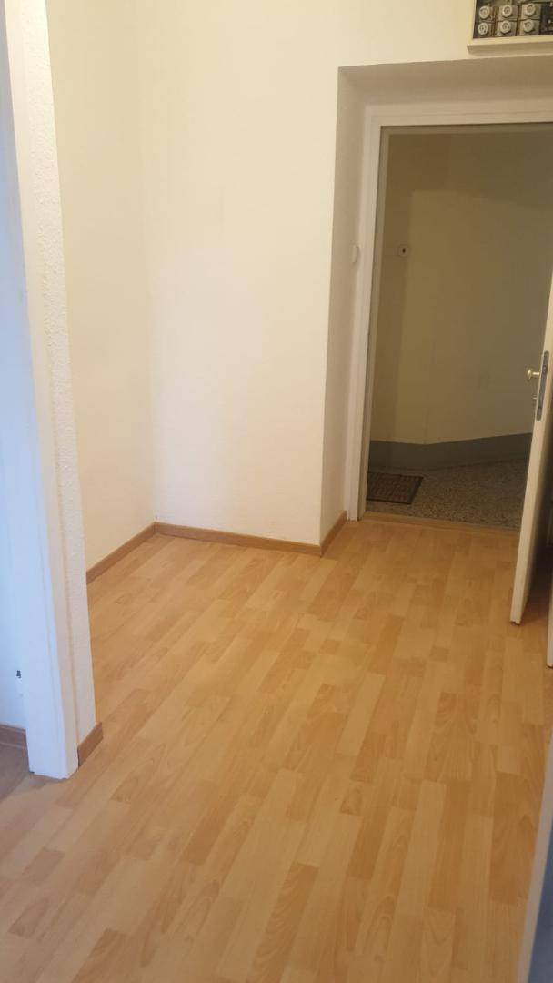 Schlichter Flur mit hellem Laminatboden und weiß gestrichenen Wänden, der zu einem weiteren Raum führt.