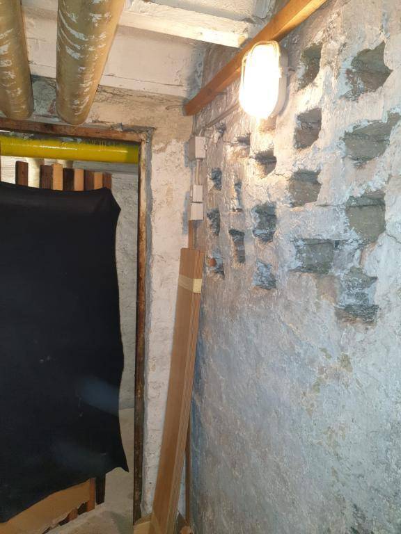 Kellerraum mit unverputzten Wänden, sichtbaren Rohren und einer einfachen Glühbirnenbeleuchtung.