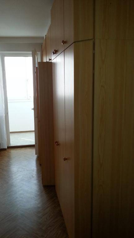 Lange Reihe von Einbauschränken aus Holz, die zu einem hellen Balkonzugang führen.