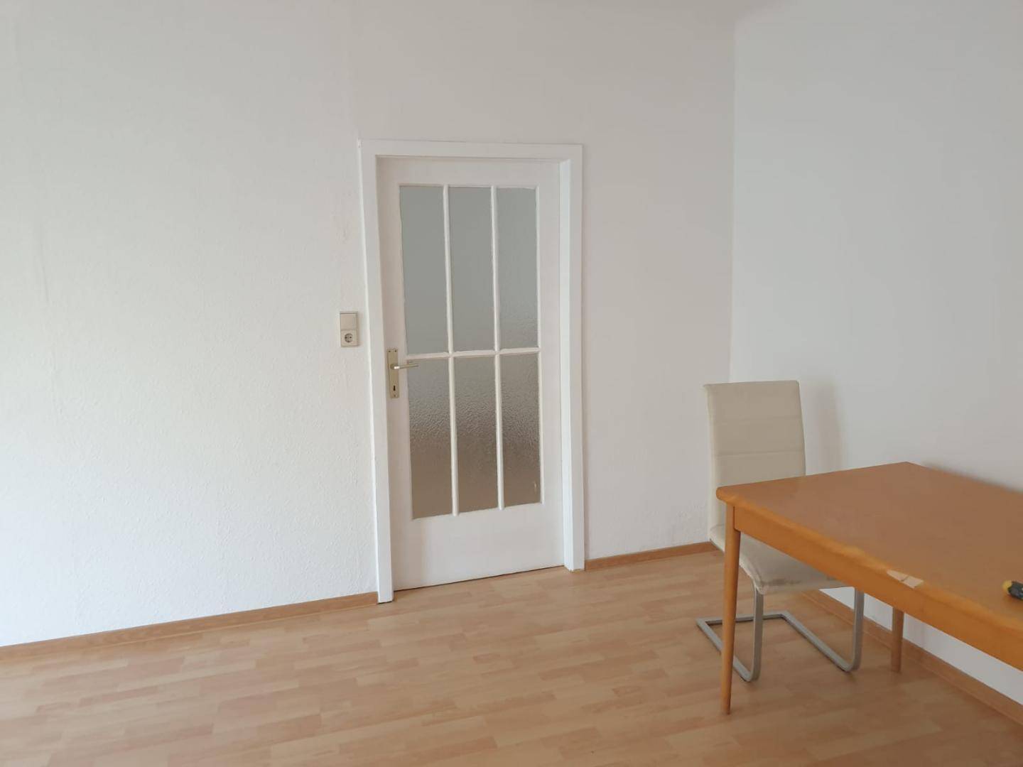 Leerer Raum mit Laminatboden und einer Tür mit Glaseinsätzen.