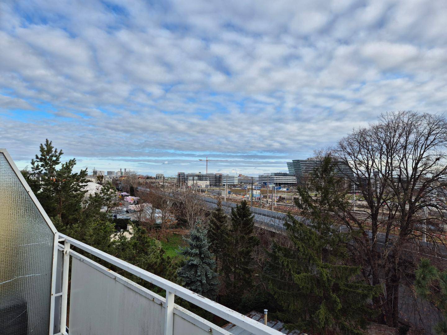 Aussicht vom Balkon mit Blick auf Bäume, Bahngleise und die städtische Skyline.