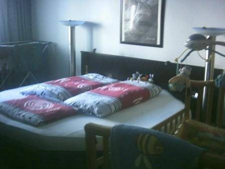 Schlafzimmer mit einem Doppelbett und einem Kinderbett, in gedämpftem Licht.