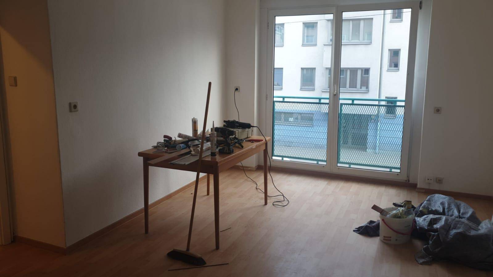 Heller Wohnraum mit Laminatboden und Zugang zu einem Balkon, derzeit in Renovierung.