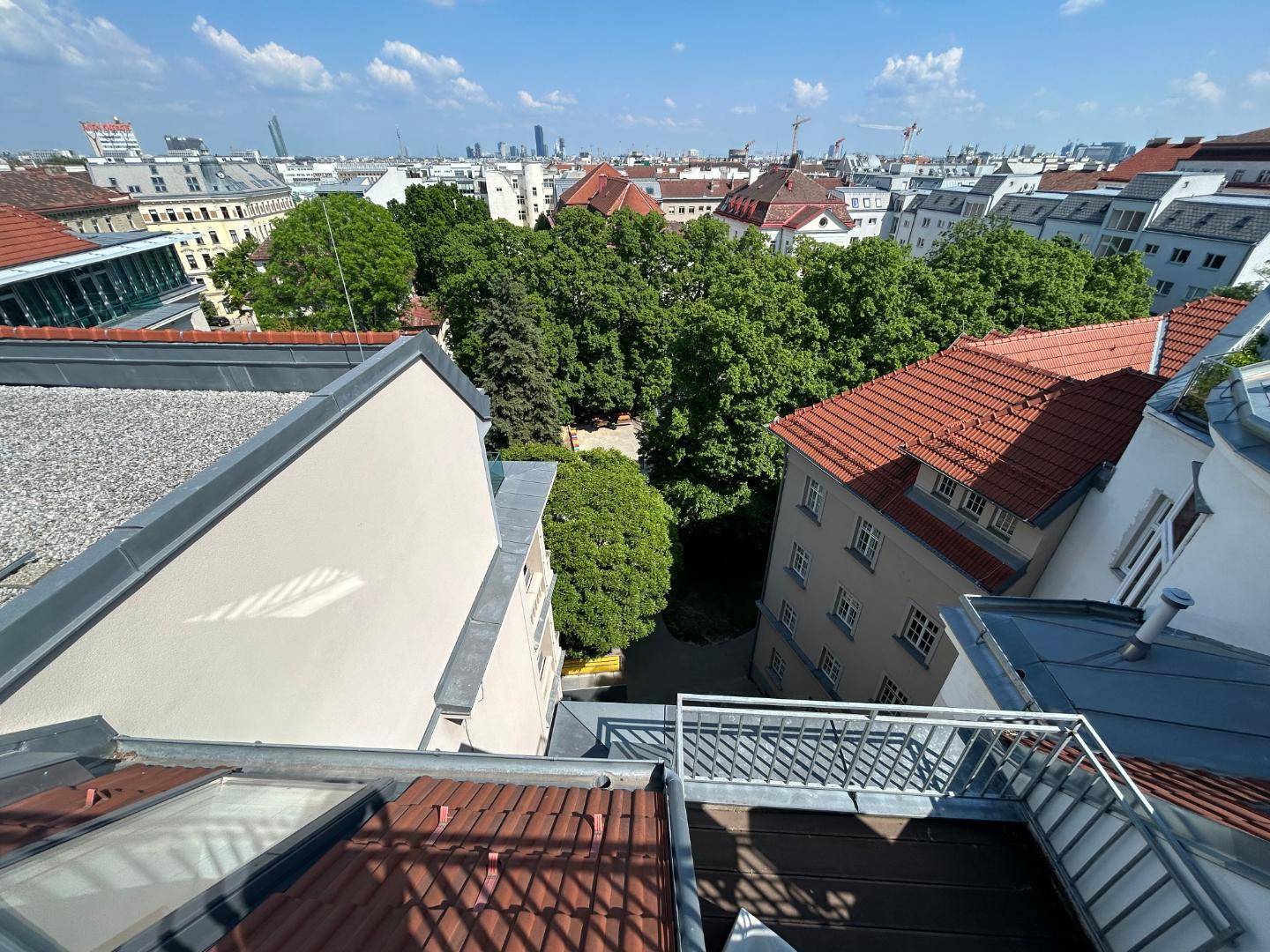 Blick von oben auf einen grünen Innenhof, umgeben von städtischen Gebäuden und Dächern.