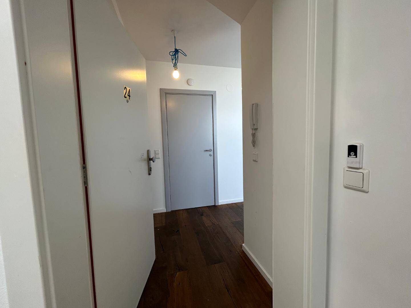 Heller Eingangsbereich mit Holzboden und Gegensprechanlage, der zur Wohnung führt.