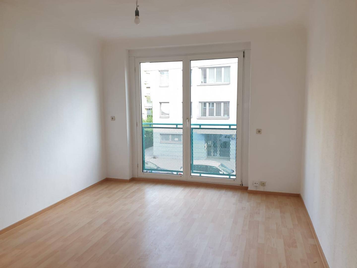 Geräumiges Wohnzimmer mit hellem Laminatboden und großer Balkontür für viel Licht.