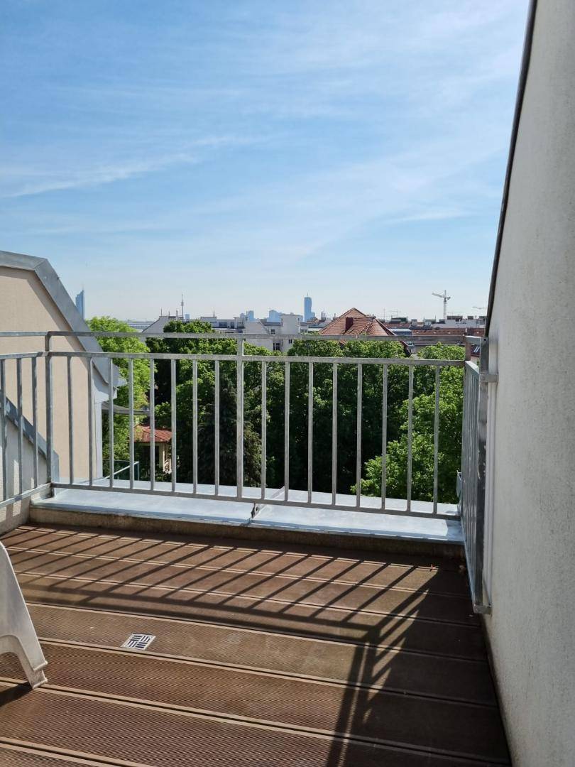Kleiner Balkon mit Holzboden und Blick auf die grüne Stadtlandschaft.
