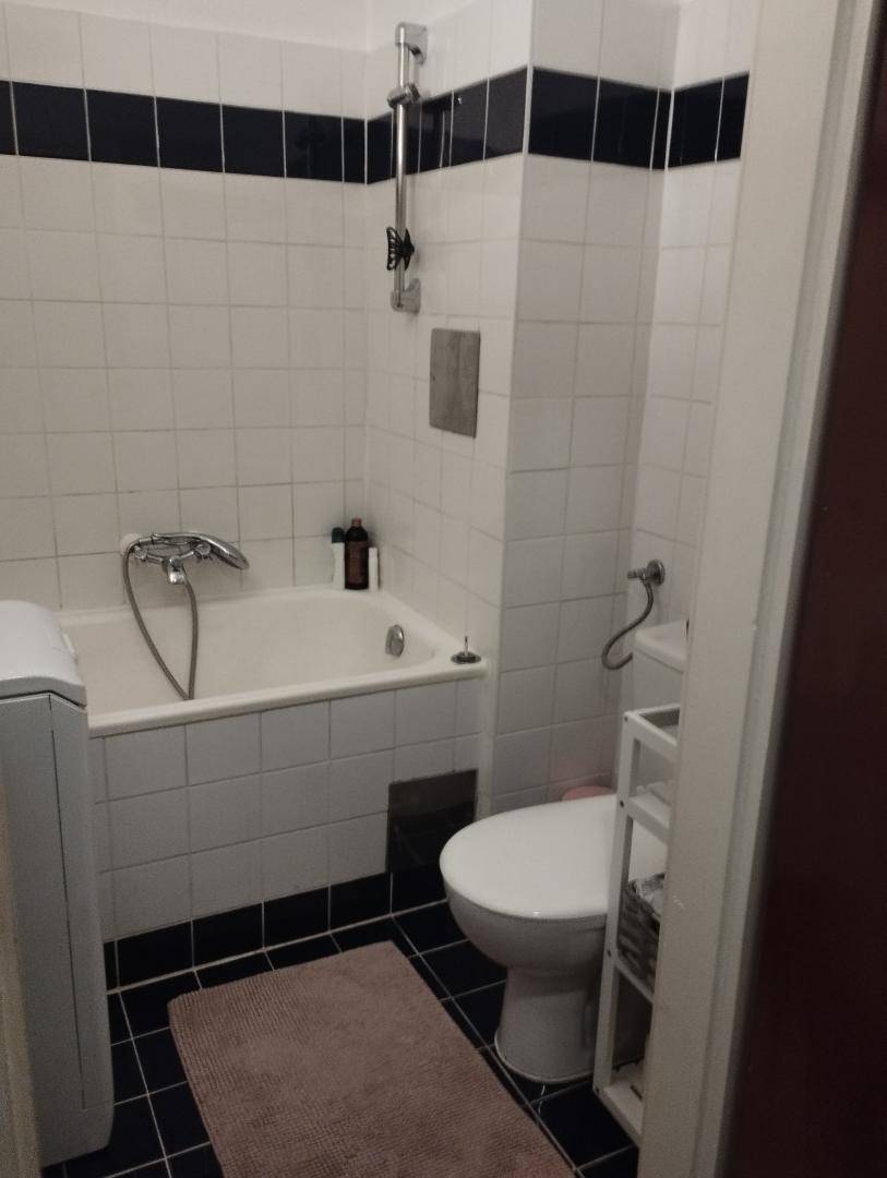 Badezimmer mit Badewanne, Toilette und Waschmaschine, gefliest in Weiß und Schwarz.