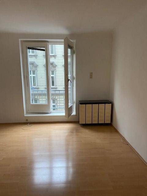 Leerer Raum mit Fenstertür und einem kleinen Heizkörper, der auf die Straße blickt.