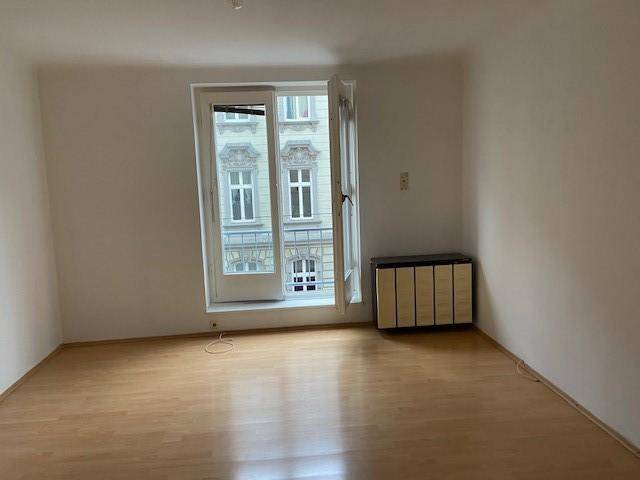 Geräumiger, leerer Raum mit Holzfußboden und einer Fenstertür, die viel Licht spendet.