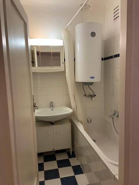 Badezimmer mit Badewanne, Waschbecken und einem Warmwasserboiler an der Wand.