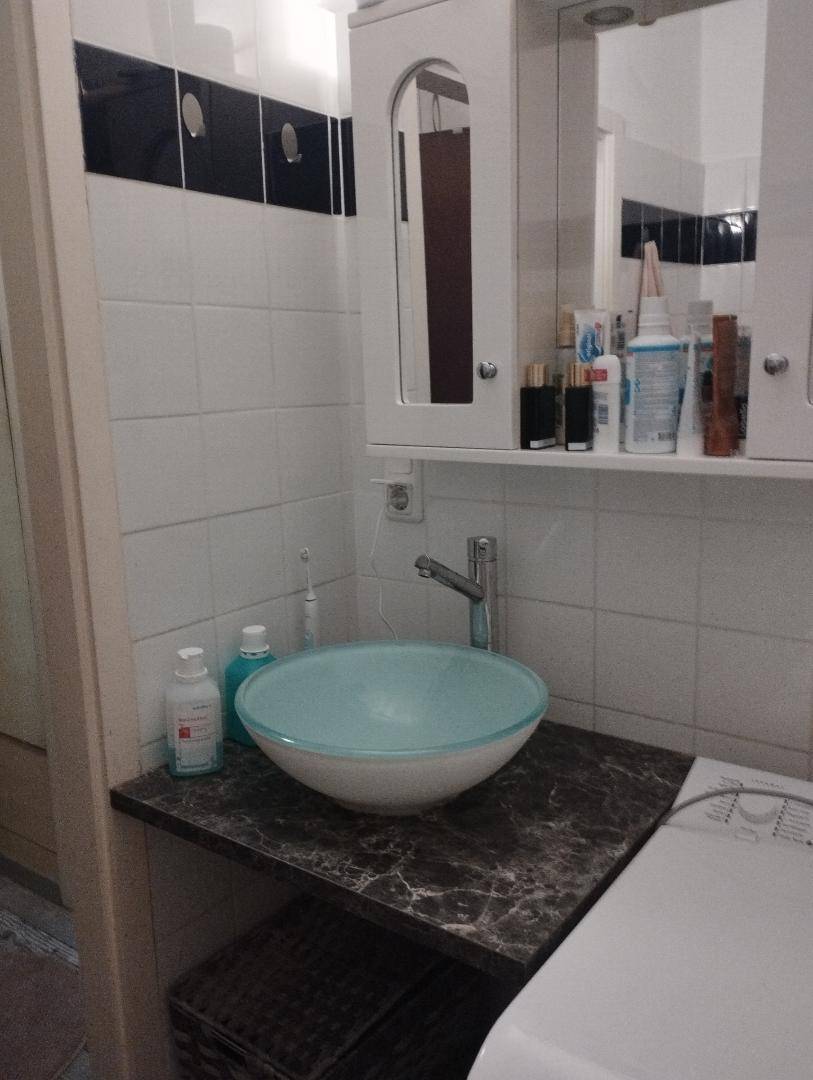 Badezimmer mit modernem Aufsatzwaschbecken, Spiegelschrank und Waschmaschine unter der Ablage.