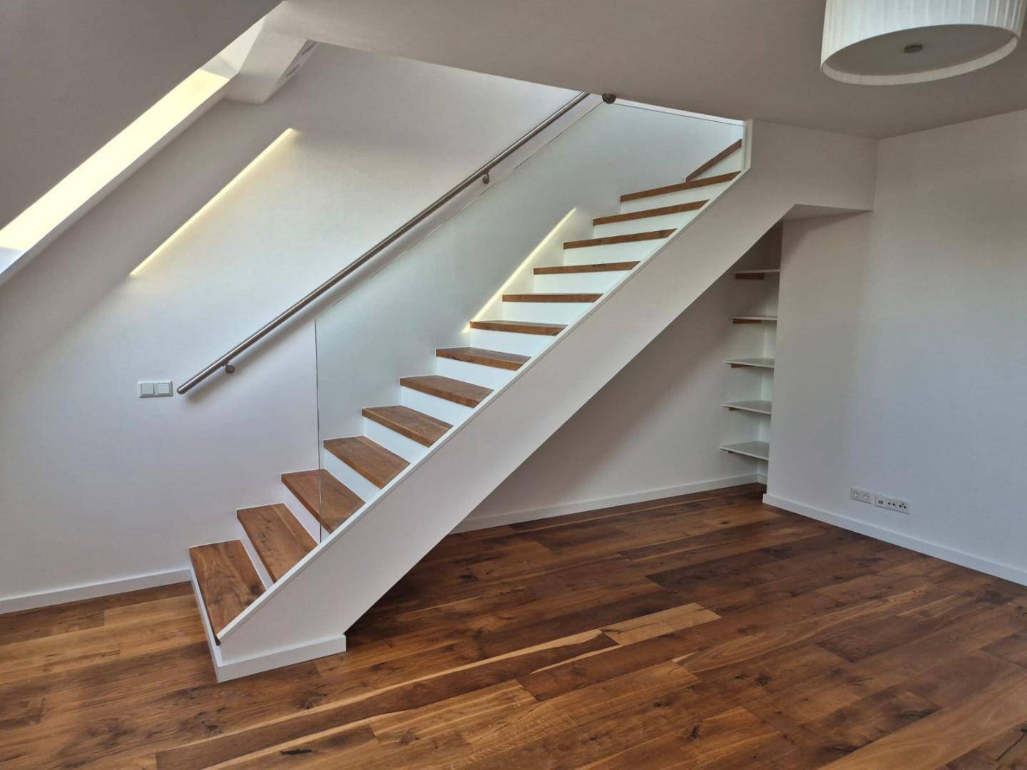 Moderne Holztreppe mit weißem Geländer und integrierter Beleuchtung, führt in die obere Etage.