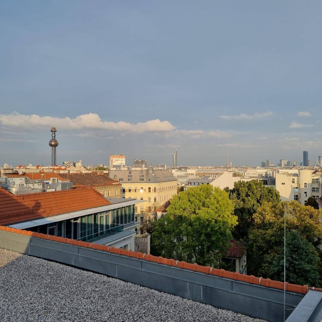 Weitläufiger Blick über die Stadt mit grünen Bäumen und markantem Fernsehturm am Horizont.