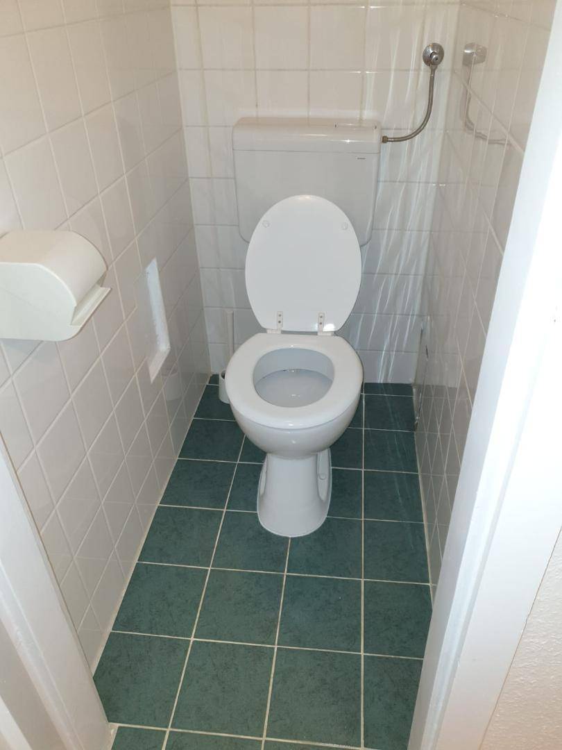 Kleines, gefliestes WC mit weißer Toilette und grünen Bodenfliesen, sauber und funktional.