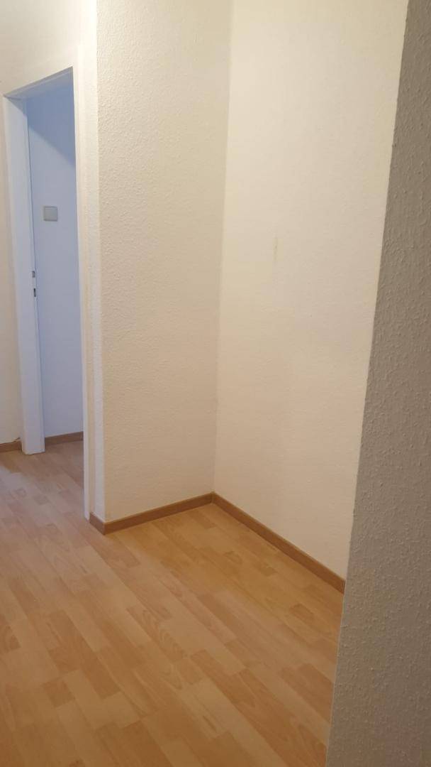 Schlichter Flur mit hellem Laminatboden und weißen Wänden, bereit zur individuellen Gestaltung.