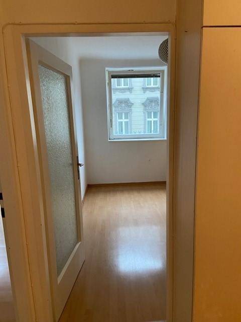 Leeres Zimmer mit Parkettboden und einem Fenster, das einen Blick auf die gegenüberliegende Fassade bietet.