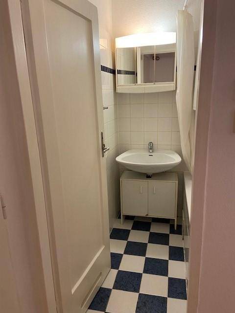 Kleines Badezimmer mit Waschbecken, Spiegelschrank und kariertem Boden in Blau und Weiß.