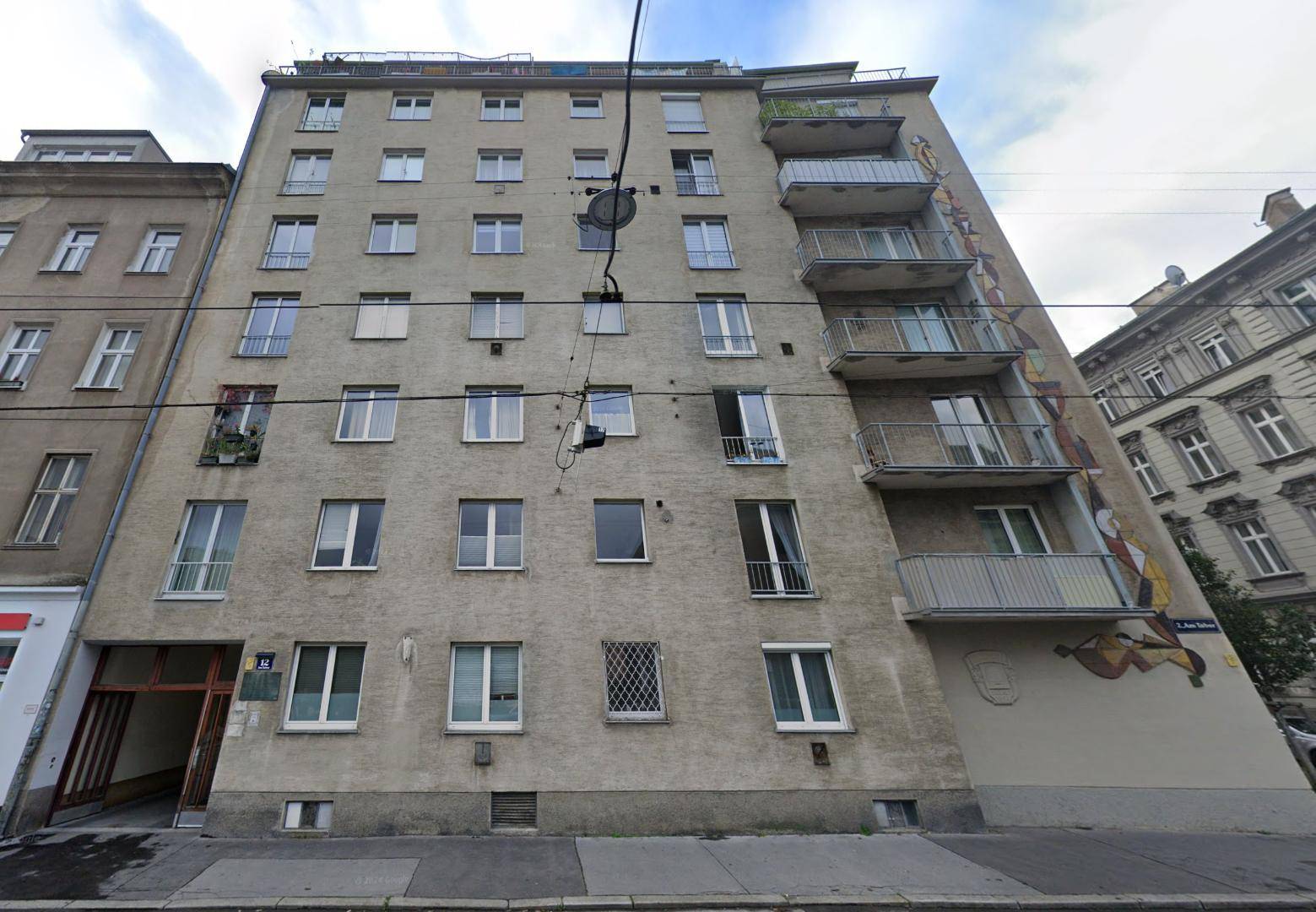 Mehrstöckiges Wohngebäude mit Balkonen und einer bemalten Fassade an einem sonnigen Tag.