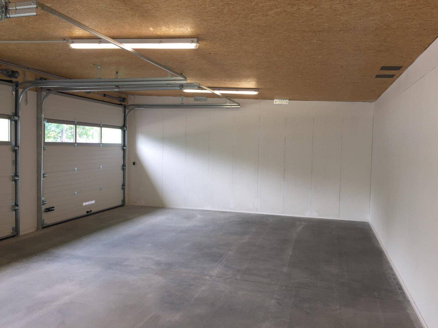 Geräumiger Garageninnenraum mit Betonboden, Holzdach und geöffnetem Rolltor.