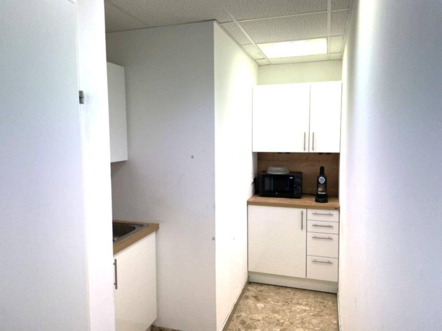 Schmale Küchenzeile mit weißen Schränken, Mikrowelle und Spülbecken in einem Flurbereich.