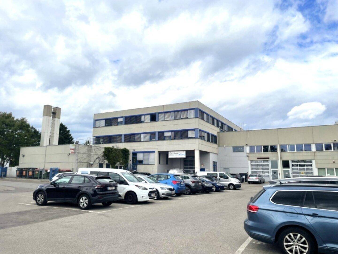 Großes Geschäftsgebäude mit Parkplätzen davor unter bewölktem Himmel.