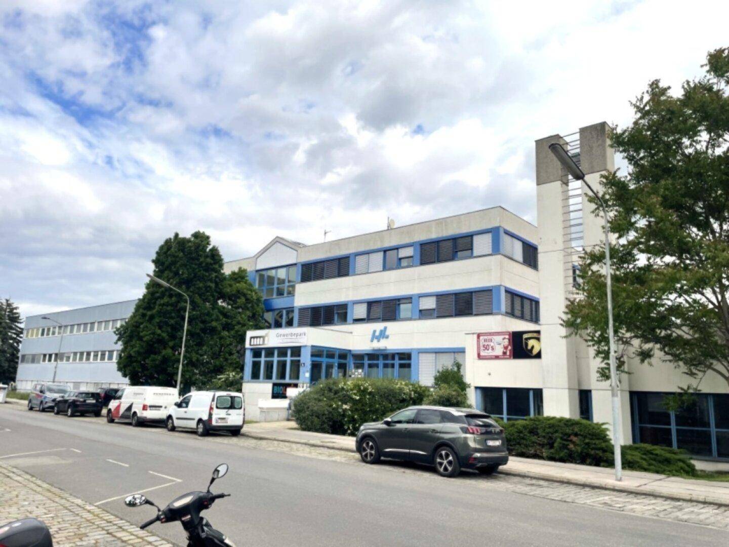 Ansicht eines modernen Geschäftsgebäudes von der Straße mit Bäumen und geparkten Autos.