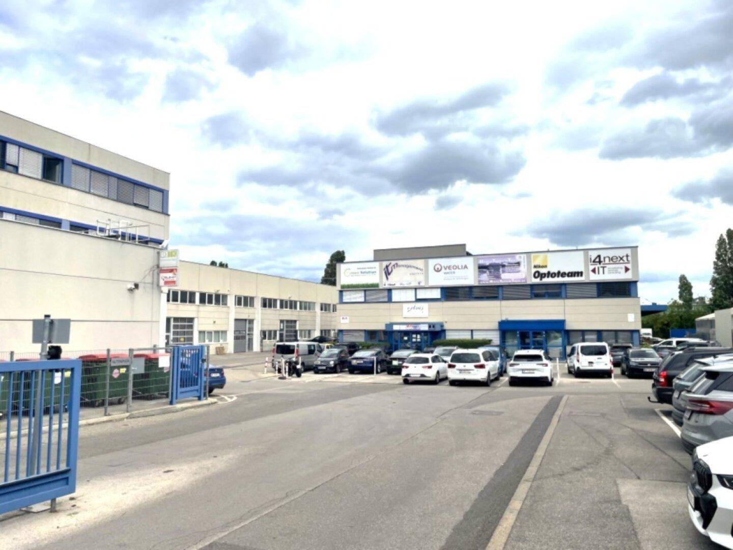 Weitläufiger Gewerbekomplex mit mehreren Gebäuden und großem Parkplatz unter bewölktem Himmel.