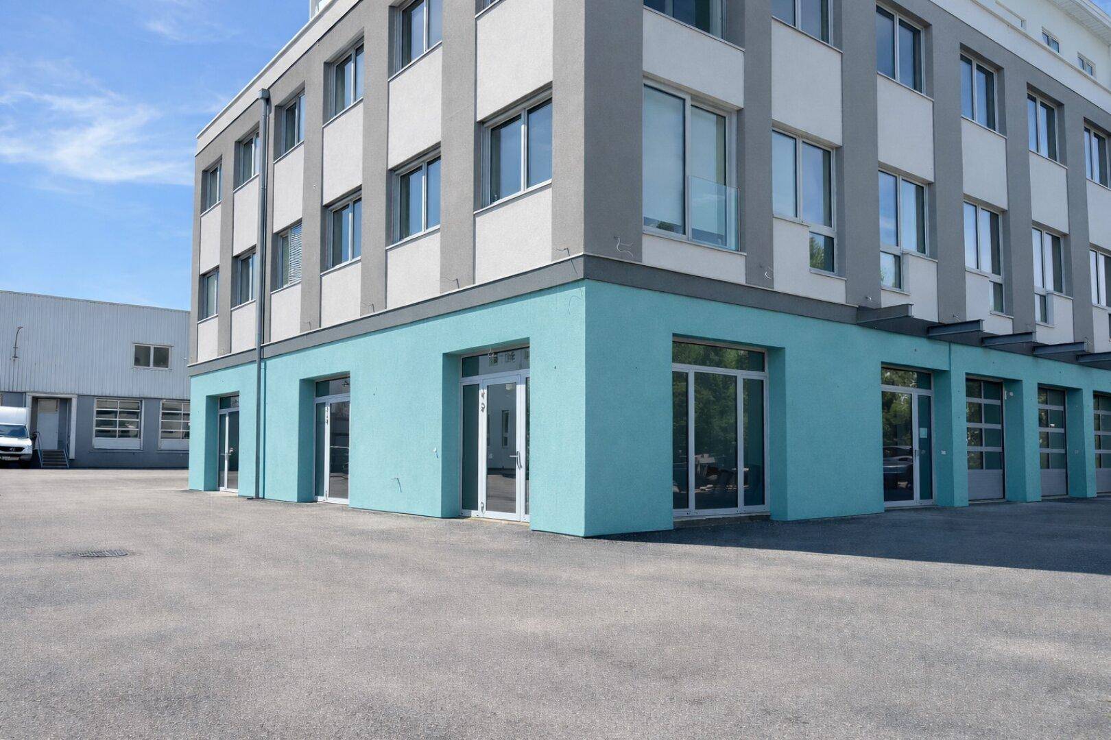 Ansicht des modernen Geschäftsgebäudes mit hellblauer Fassade und großzügigen Fensterfronten unter blauem Himmel.