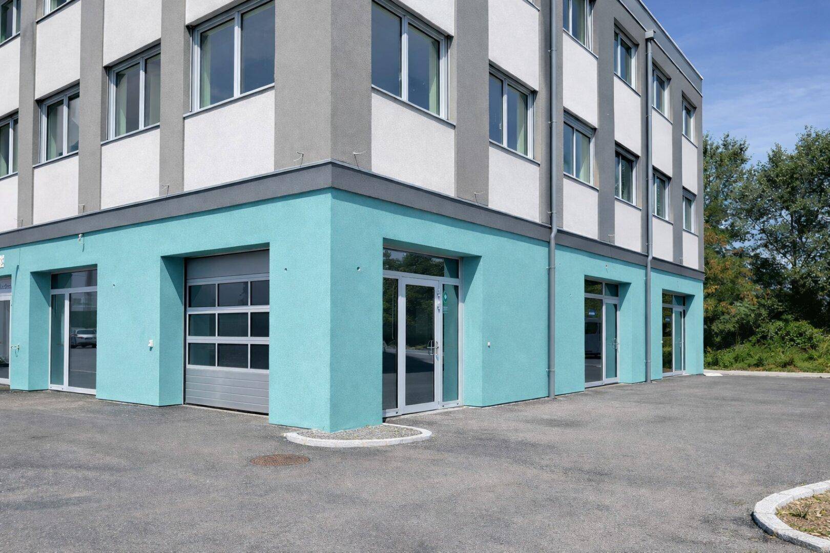Modernes Geschäftsgebäude mit hellblauer Fassade im Erdgeschoss und großen Fenstern in den oberen Etagen.