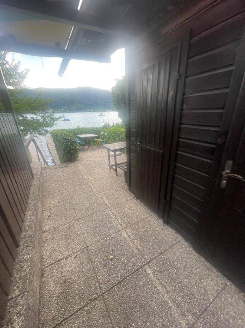 Gepflasterter Weg mit Seeblick und kleinem Sitzbereich vor einer Holzhütte.