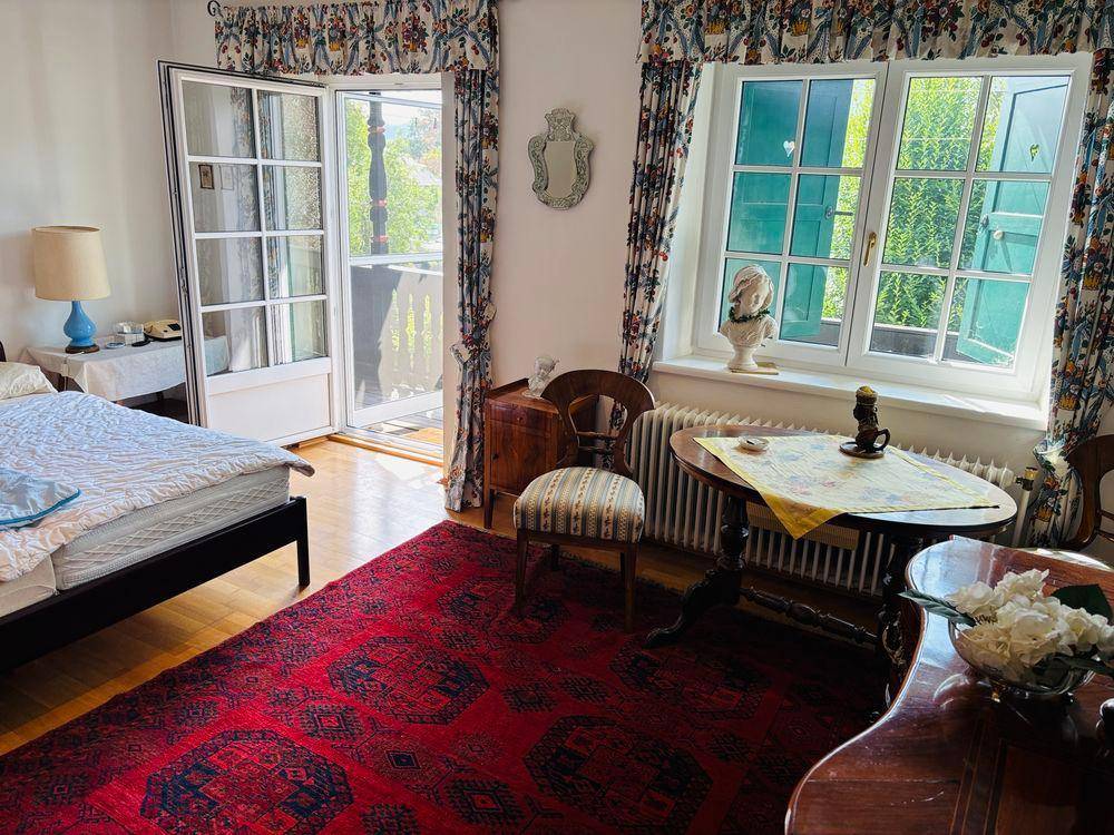 Helles Schlafzimmer mit Holzboden, traditionellen Möbeln und Zugang zum Balkon.