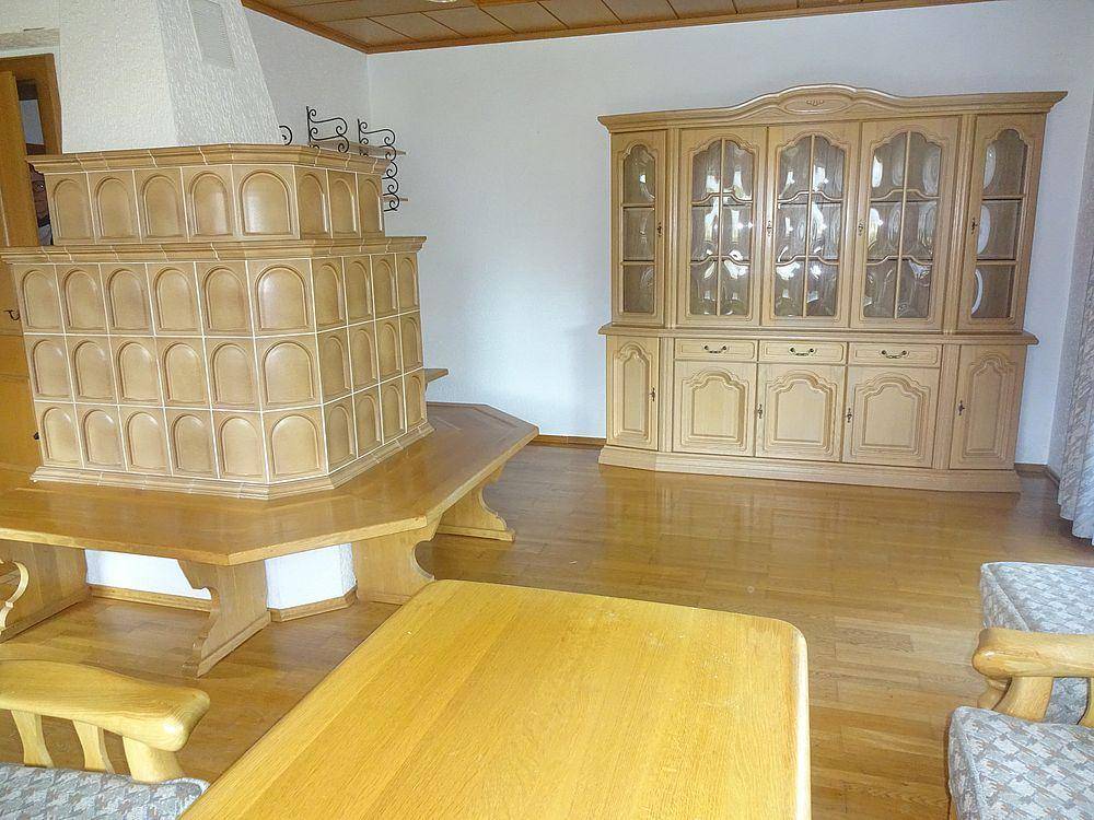 Wohnzimmer mit traditionellem Kachelofen, Holzparkett und einem großen Holzschrank.